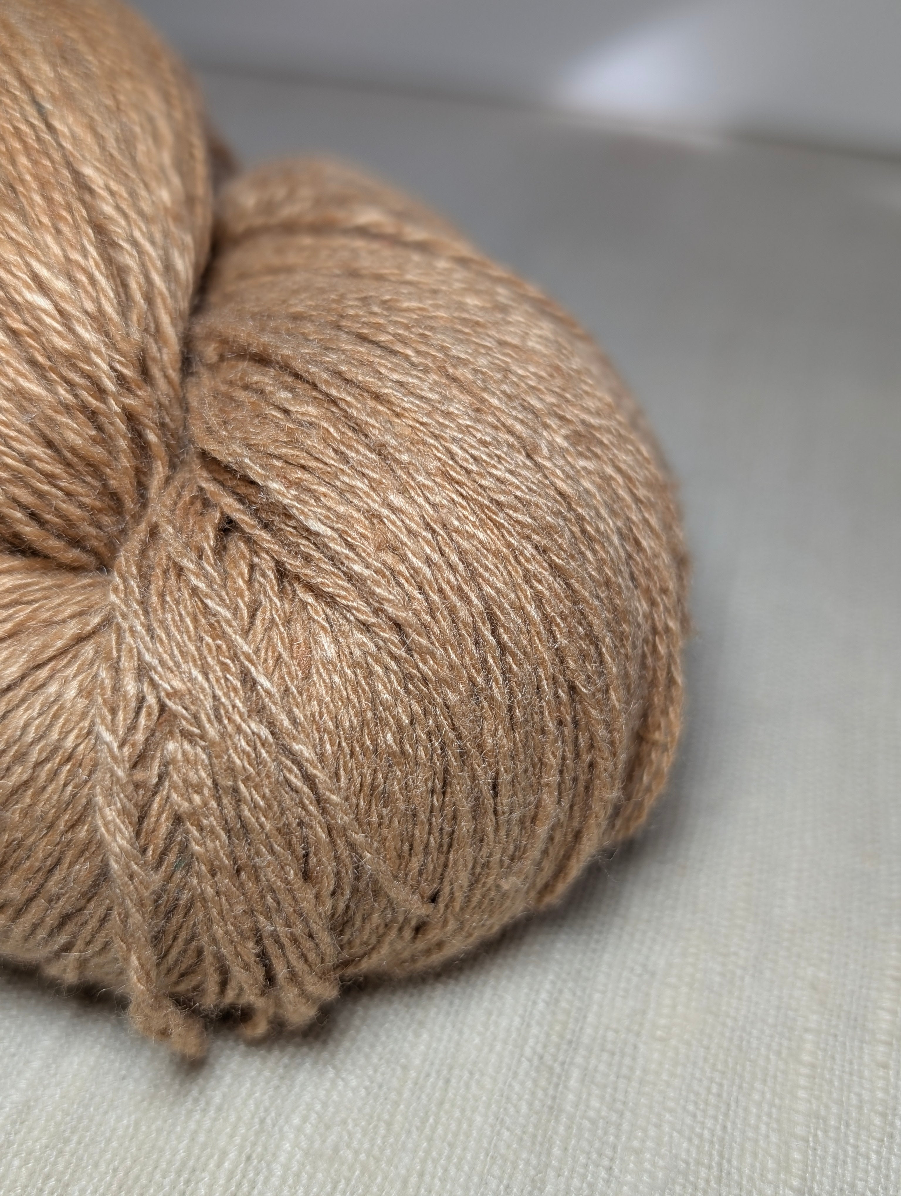 Close-up of a skein of warm golden amber coloured naturally dyed Eri silk, sitting on a piece of hand-loomed Eri silk fabric.  