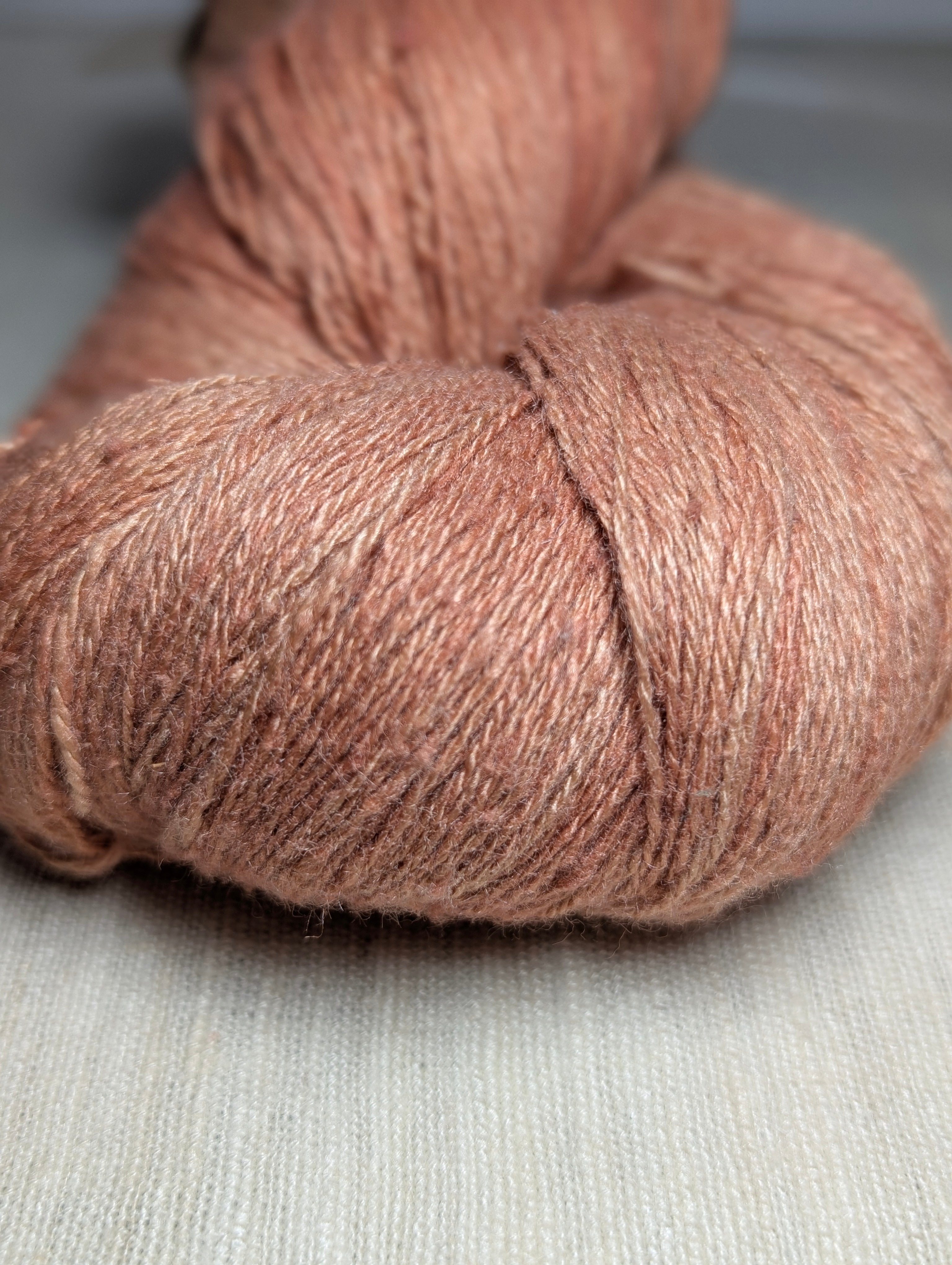 Close-up of softly variegated naturally dyed Eri silk yarn in shades of coral, salmon, and apricot. The skein is sitting on a piece of undyed hand-loomed Eri silk fabric.