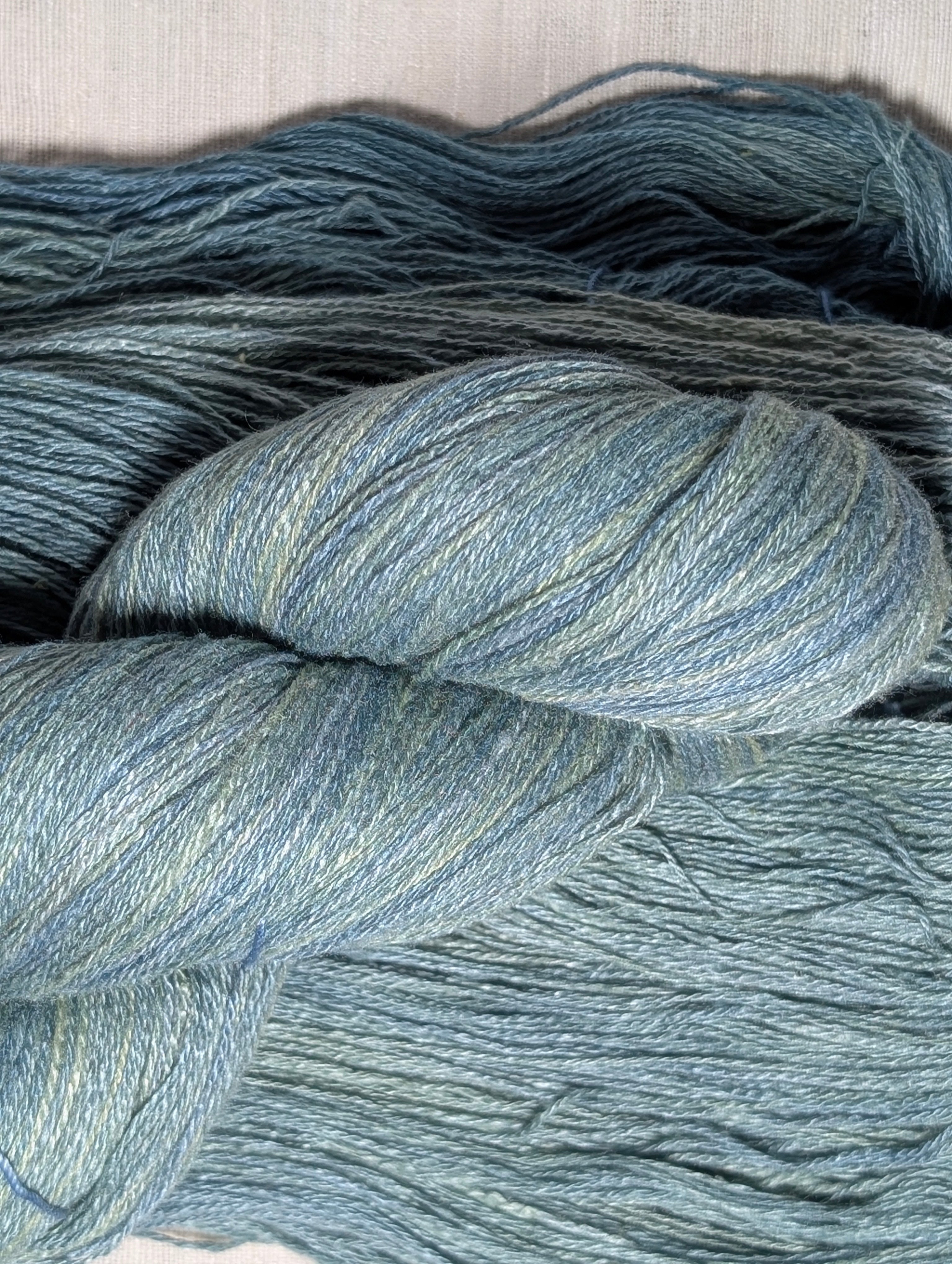 A twisted skein of undulating teal yarn laid on top of an unbound skein. 