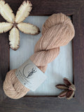 Warm golden amber coloured skein of naturally dyed Eri silk yarn with a label surrounded by a rustic wooden frame accented with seed pods of the Australian teak tree.