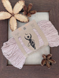 5-ply/Sport Eri silk yarn in pale lavender-grey, wrapped in a kraft label, on a piece of undyed Eri silk fabric in a rustic hand-made dark wooden frame accented with seed pods from the Australian teak tree⠋