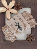 Imperial Topaz 5-ply/Sport Eri silk yarn in variegated brown, cream and grey, wrapped in a kraft label, on a piece of undyed Eri silk fabric in a rustic hand-made dark wooden frame accented with seed pods from the Australian teak tree