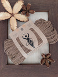 Cocoa 5-ply/Sport Eri silk yarn in rich chocolate-brown tones, wrapped in a kraft label, on a piece of undyed Eri silk fabric in a rustic hand-made dark wooden frame accented with seed pods from the Australian teak tree.